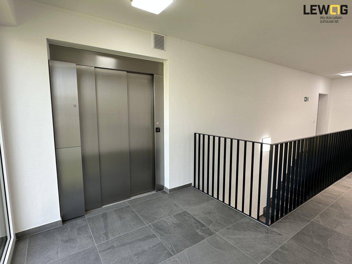 Heller Flur im Gebäude mit modernem Aufzug und Treppenhauszugang.