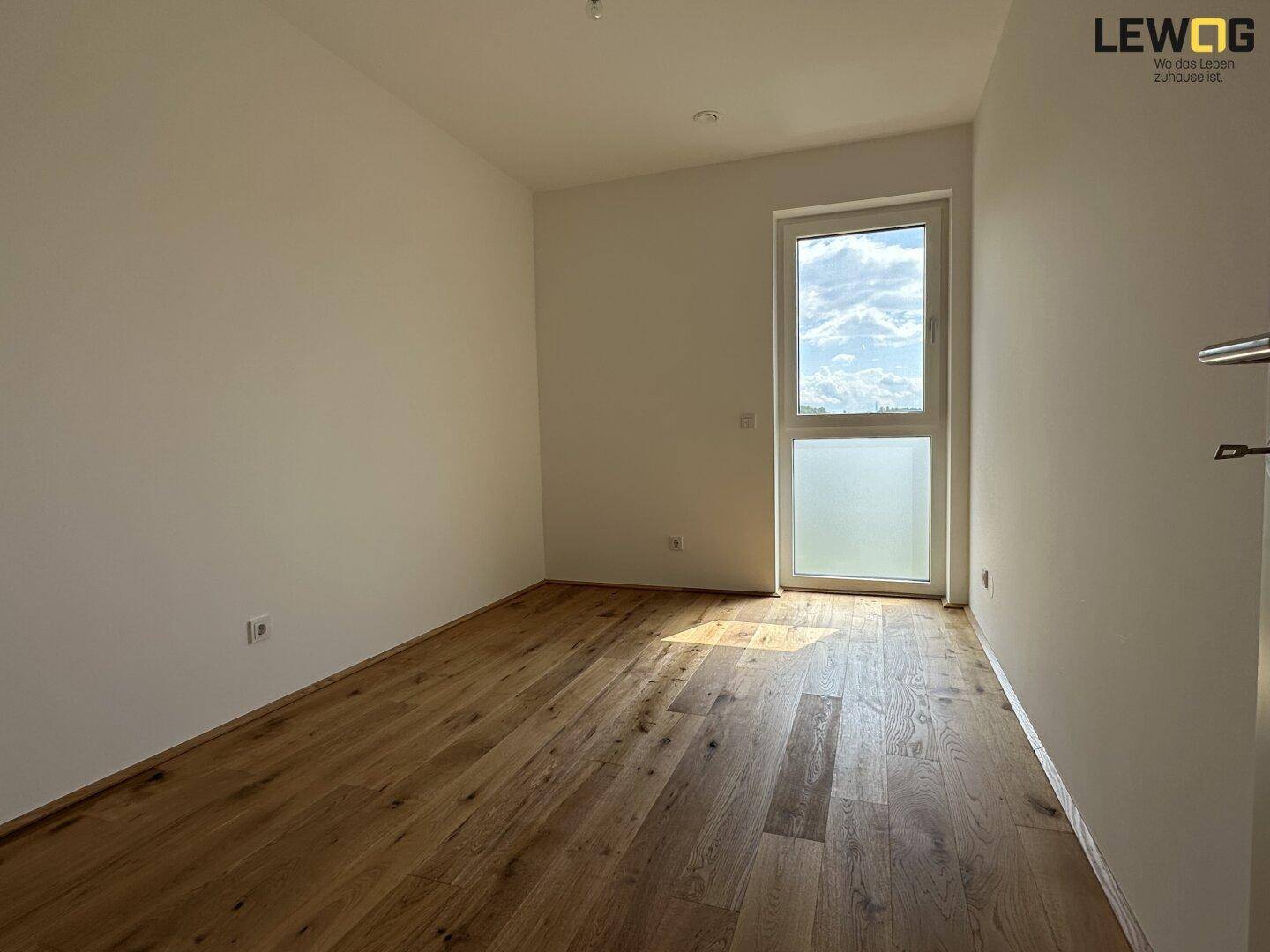 Lichtdurchflutetes Schlafzimmer mit Parkettboden und großem Fenster.