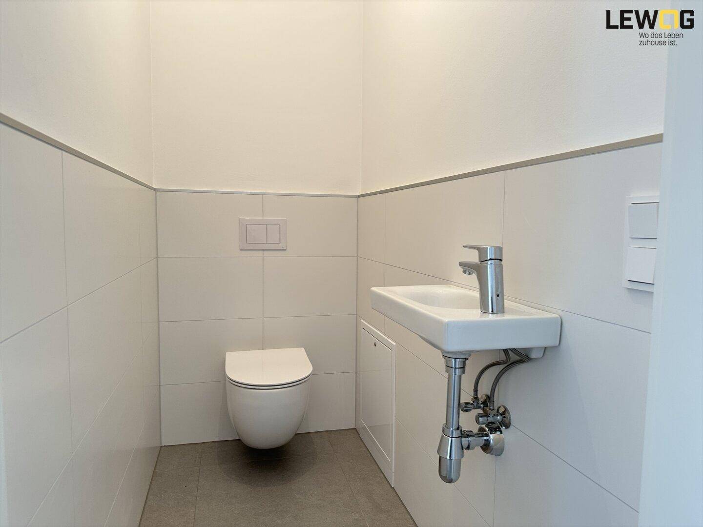 Modernes Gäste-WC mit wandhängendem WC, kleinem Waschbecken und hellen Fliesen.