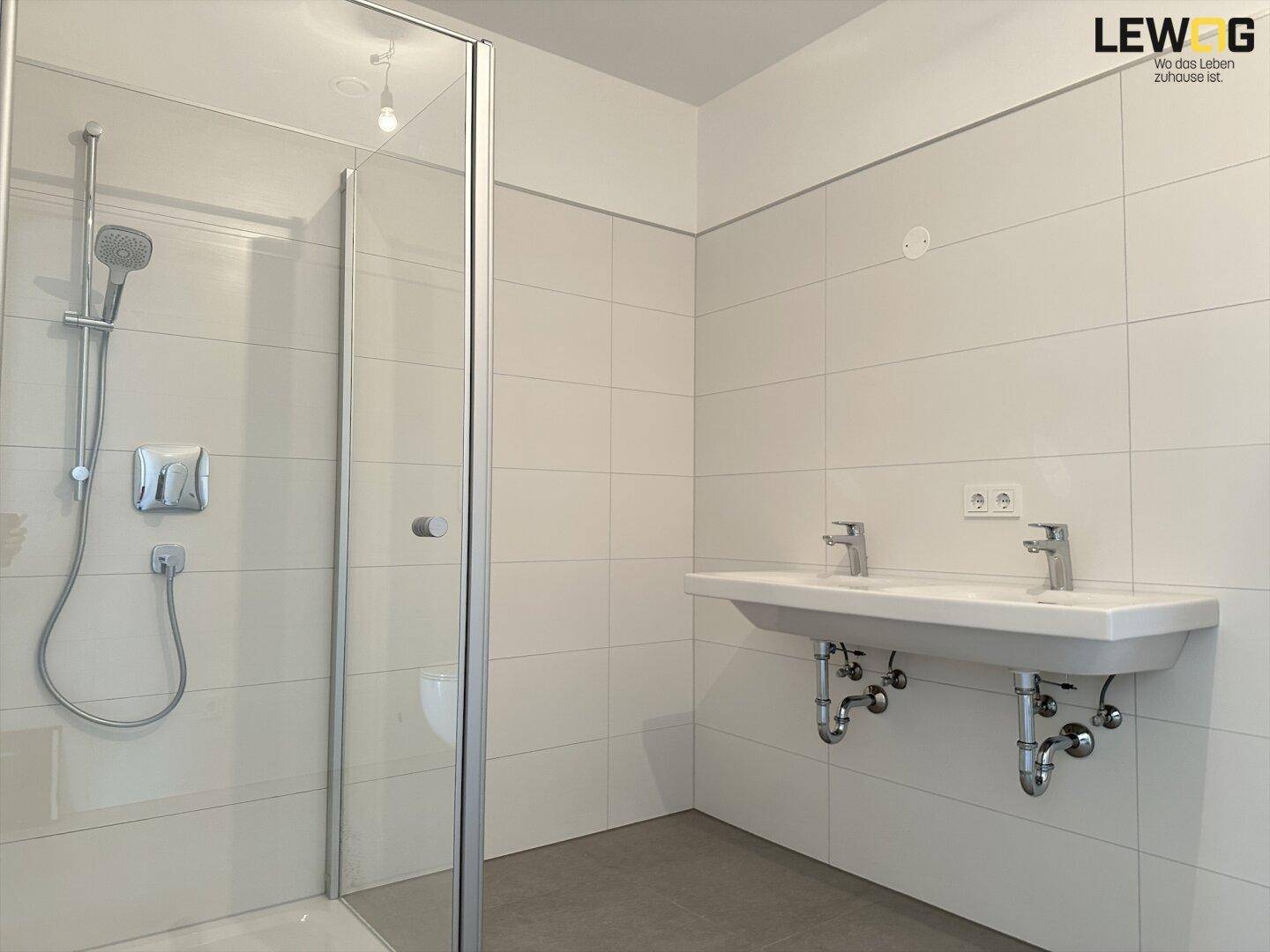 Modernes Badezimmer mit Doppelwaschbecken, großer Dusche und hellen Fliesen.