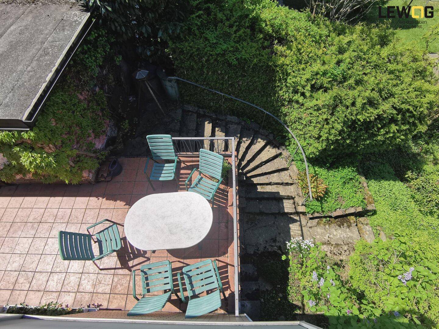Gemütliche Terrasse mit Gartenmöbeln und Steintreppe, umgeben von üppigem Grün.