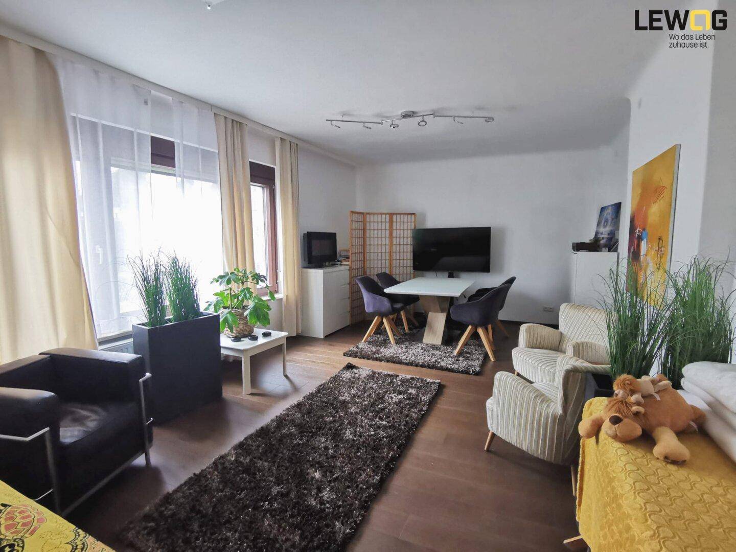 Helles Wohnzimmer mit dunklem Holzboden, bequemen Sitzgelegenheiten und einem Essbereich.