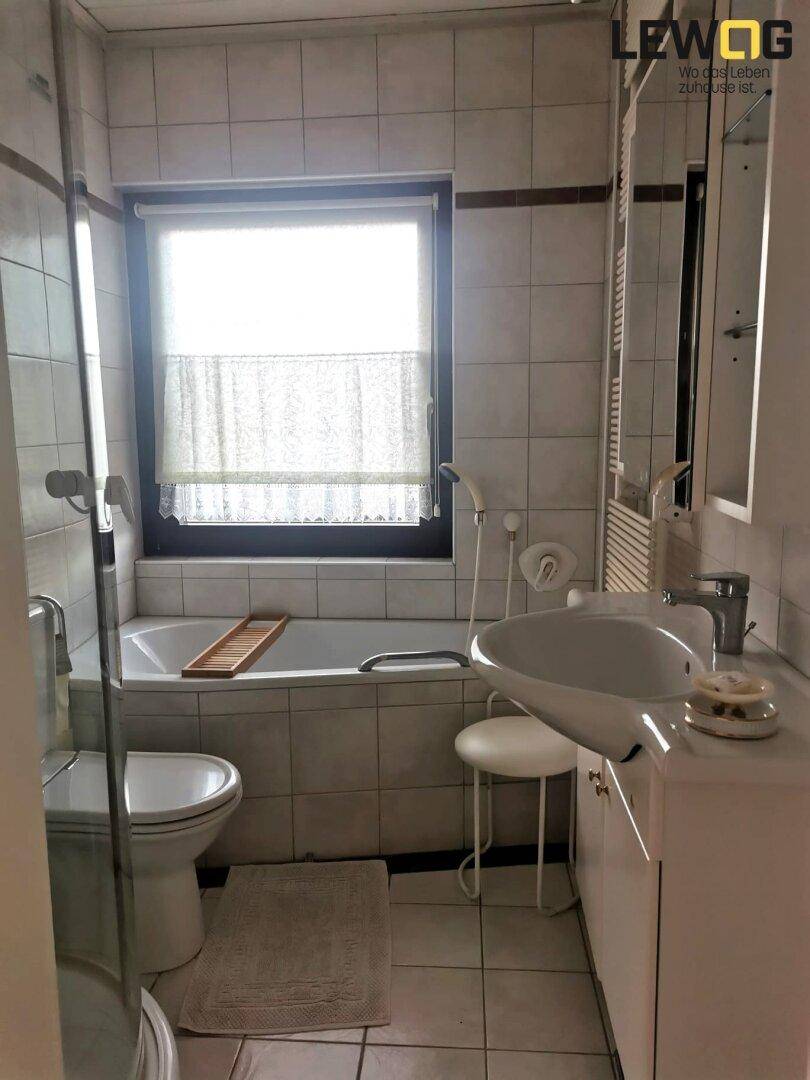 Funktionales Badezimmer mit Badewanne, Dusche, Waschbecken und Fenster für Tageslicht.