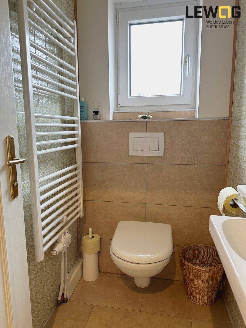 Kleines WC mit wandhängender Toilette, Waschbecken und beheiztem Handtuchhalter.