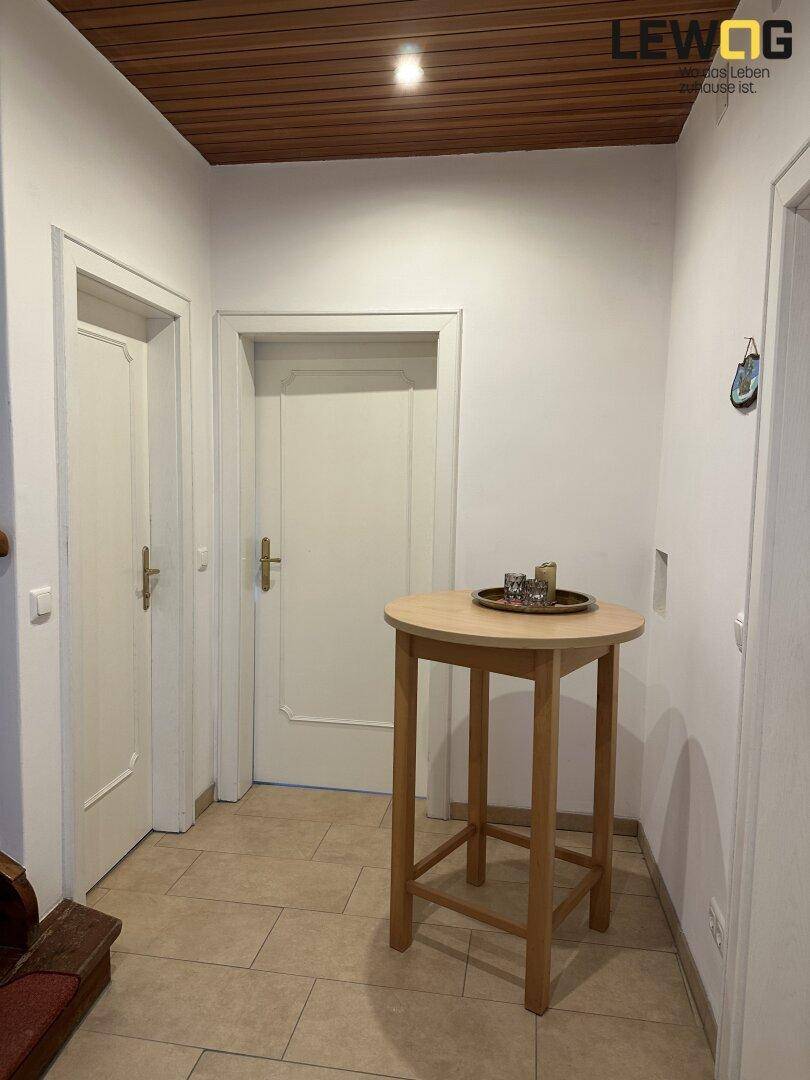 Eingangsbereich mit Fliesenboden, Holztisch und Holzdecke, der zu weiteren Räumen führt.