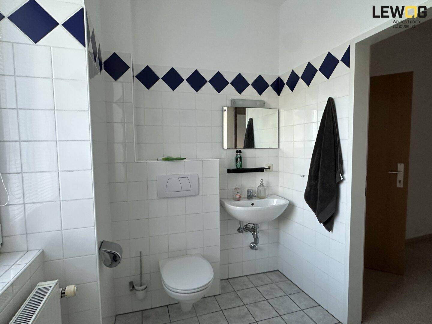 Badezimmer mit WC, Waschbecken und Spiegel, ausgestattet mit weißen Fliesen und blauen Akzenten.