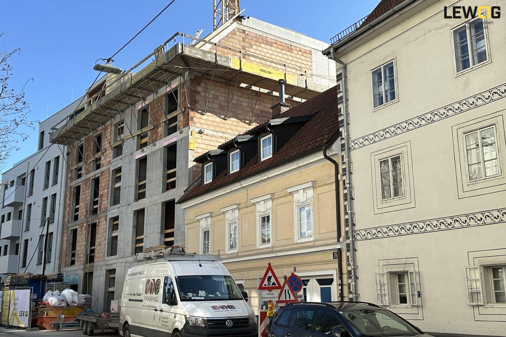Neubau im Bau neben bestehenden Gebäuden mit Gerüst und Baukran in urbaner Umgebung.