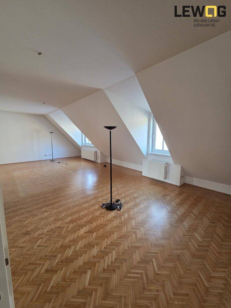 Geräumiger Dachgeschossraum mit schrägen Wänden, Parkettboden und viel natürlichem Licht.