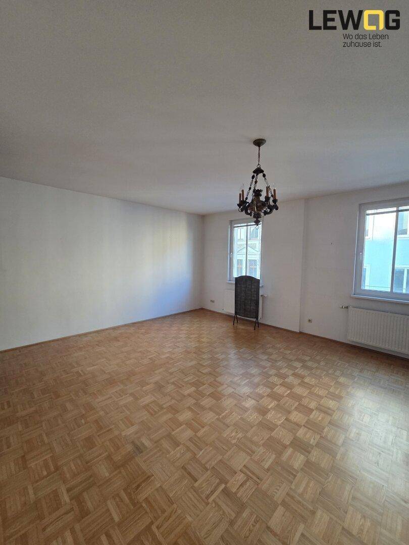 Helles Wohnzimmer mit klassischem Parkettboden und einem dekorativen Kronleuchter an der Decke.