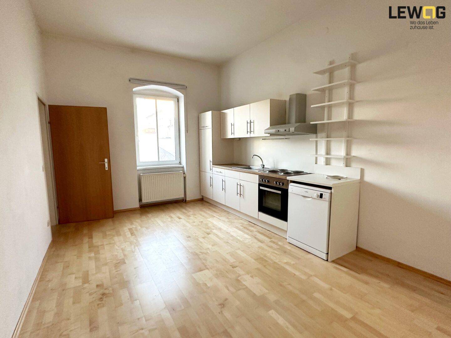Funktionale Küche mit hellen Holzschränken, Spülmaschine und Parkettboden in einem offenen Raum.