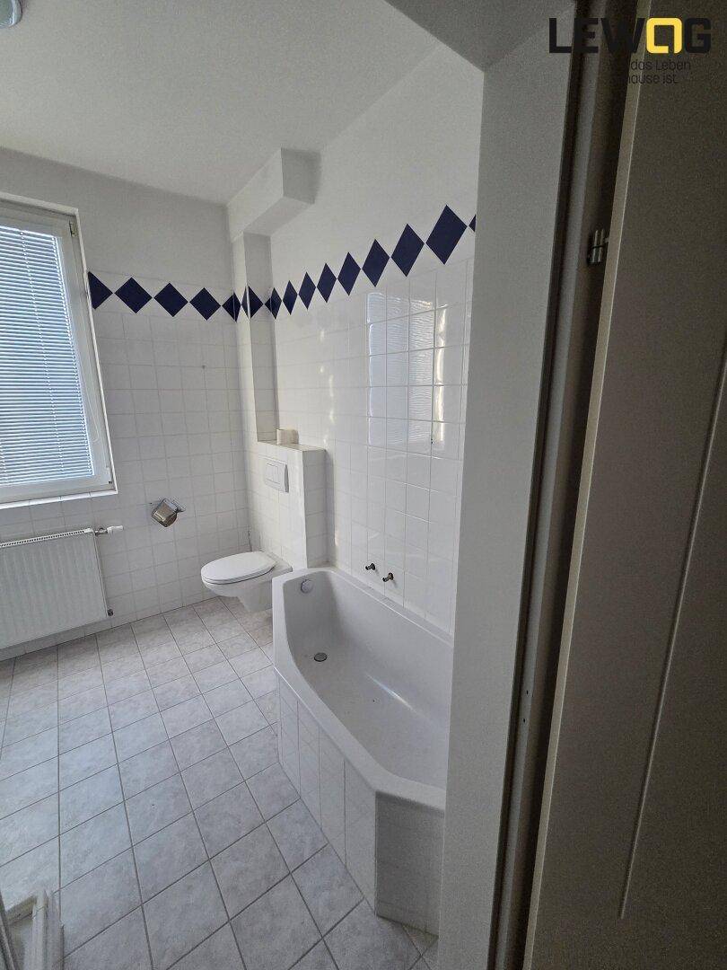 Badezimmer mit Badewanne, WC und weißen Fliesen, akzentuiert durch blaue Rautenmuster.
