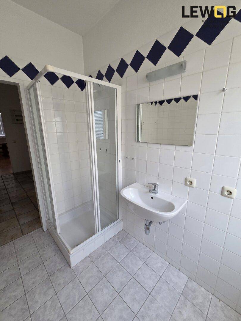 Badezimmer mit Duschkabine, Waschbecken und weißen Fliesen, verziert mit blauen Akzenten.