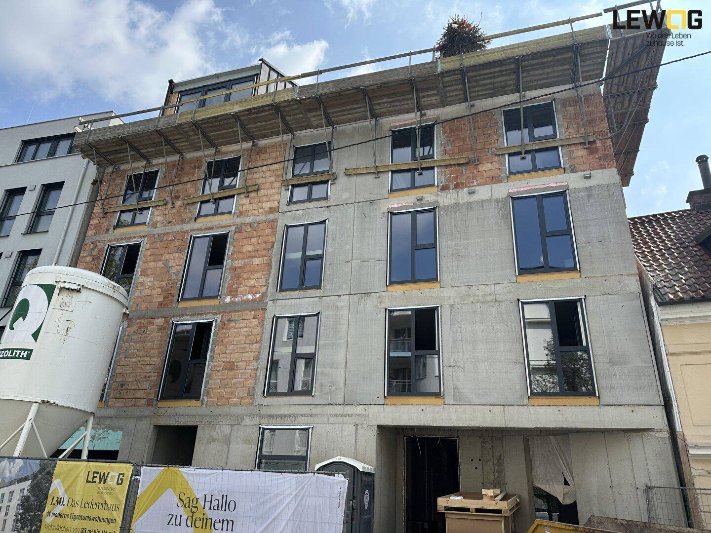 Neubau eines modernen Mehrfamilienhauses mit großen Fenstern und sichtbaren Bauelementen in städtischer Umgebung.