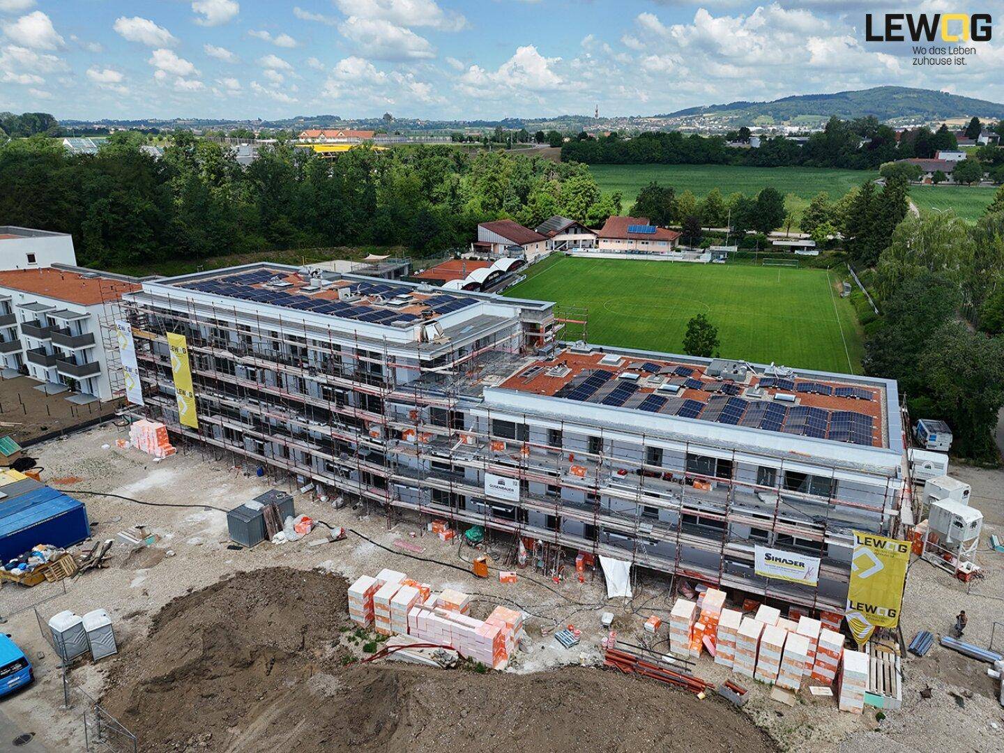 Luftaufnahme eines im Bau befindlichen Gebäudes mit Gerüst und Solaranlagen auf dem Dach.
