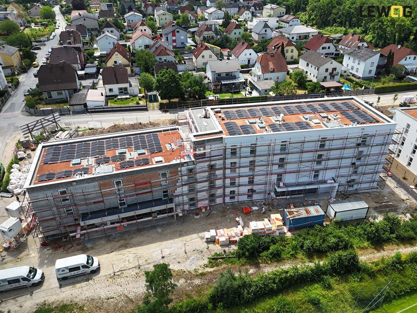 Luftaufnahme eines Neubaus mit Gerüst, Solaranlagen und umliegender Wohnbebauung.