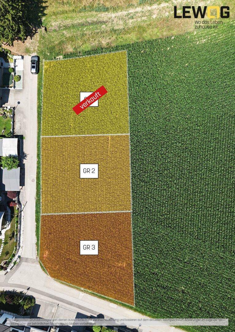 Luftaufnahme von Baugrundstücken mit angrenzenden Feldern und einer Straße, wobei ein Grundstück als verkauft markiert ist.