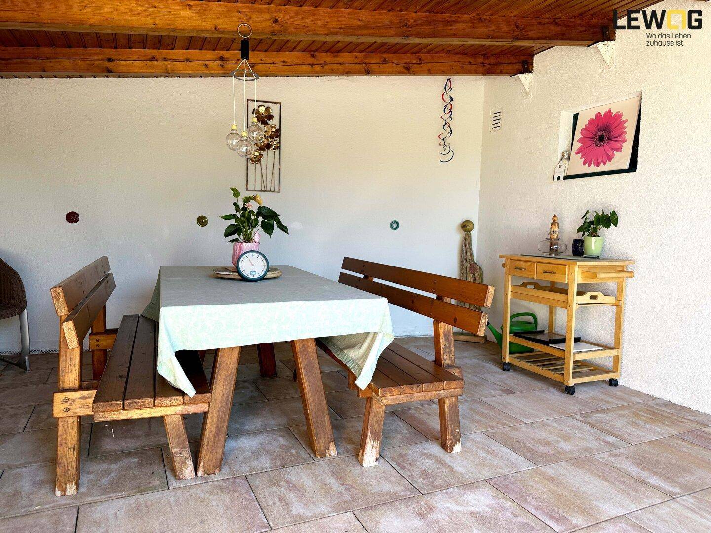Gemütlicher überdachter Essbereich im Freien mit Holztisch und Bänken, ideal für Mahlzeiten im Grünen.