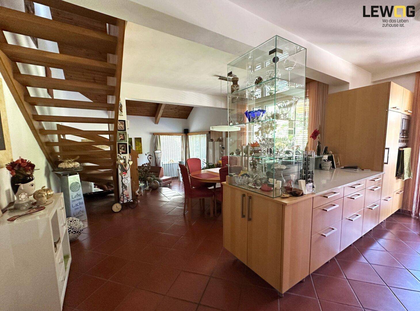 Offener Wohnbereich mit Holzküche, Essbereich und Treppe, verbunden durch Terrakotta-Fliesenboden.