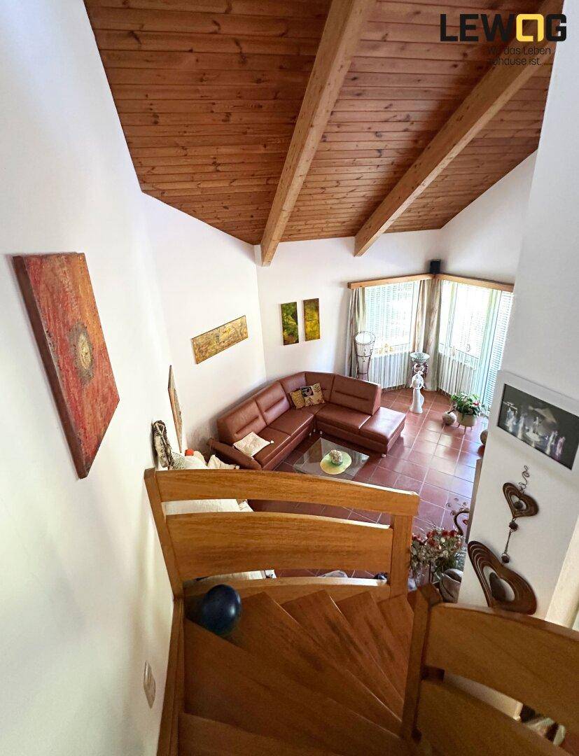 Blick von der Holztreppe in das helle Wohnzimmer mit hohen Decken und Terrakotta-Fliesenboden.