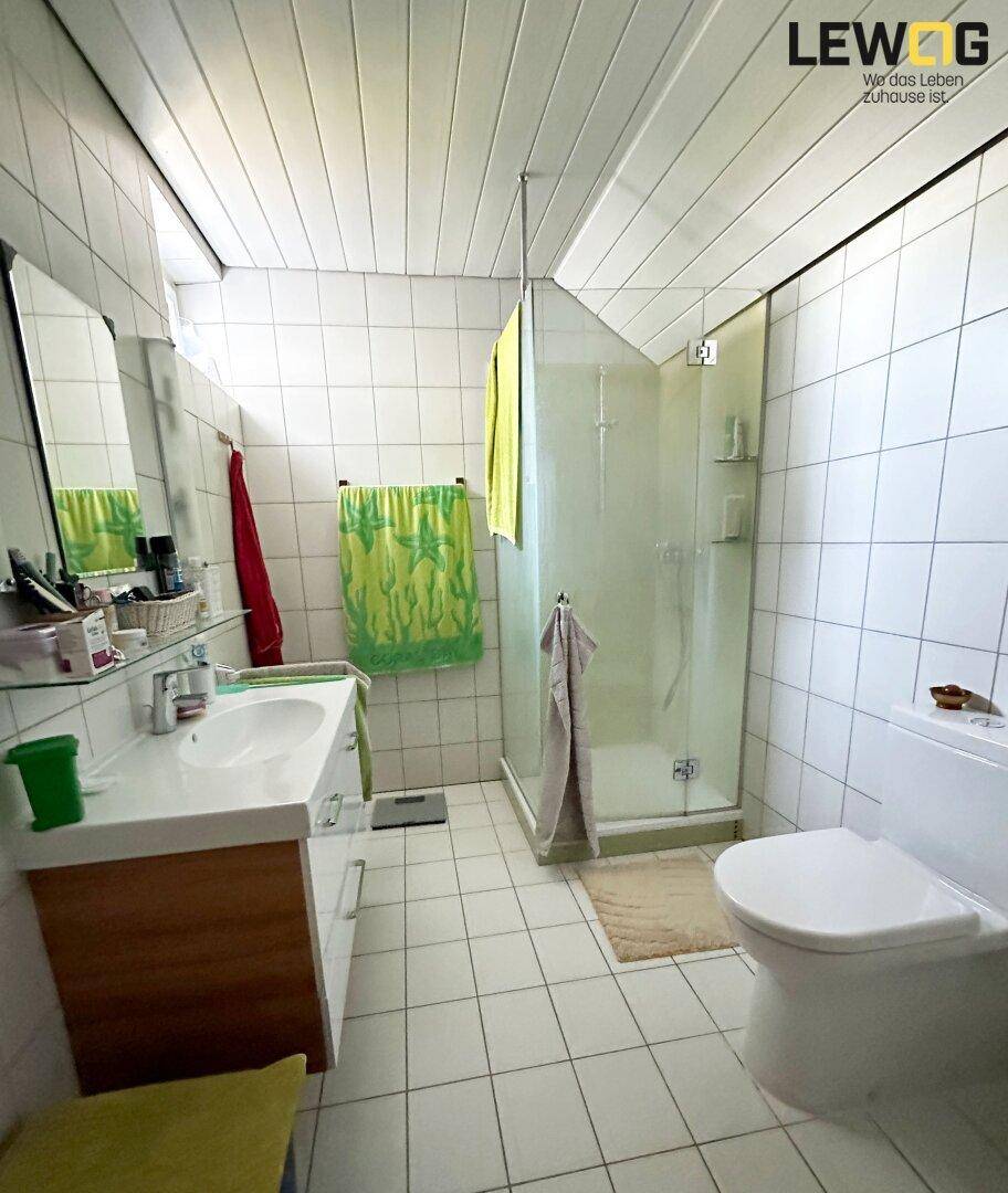 Helles Badezimmer mit weißen Fliesen, Duschkabine und Holzwaschtischunterschrank.