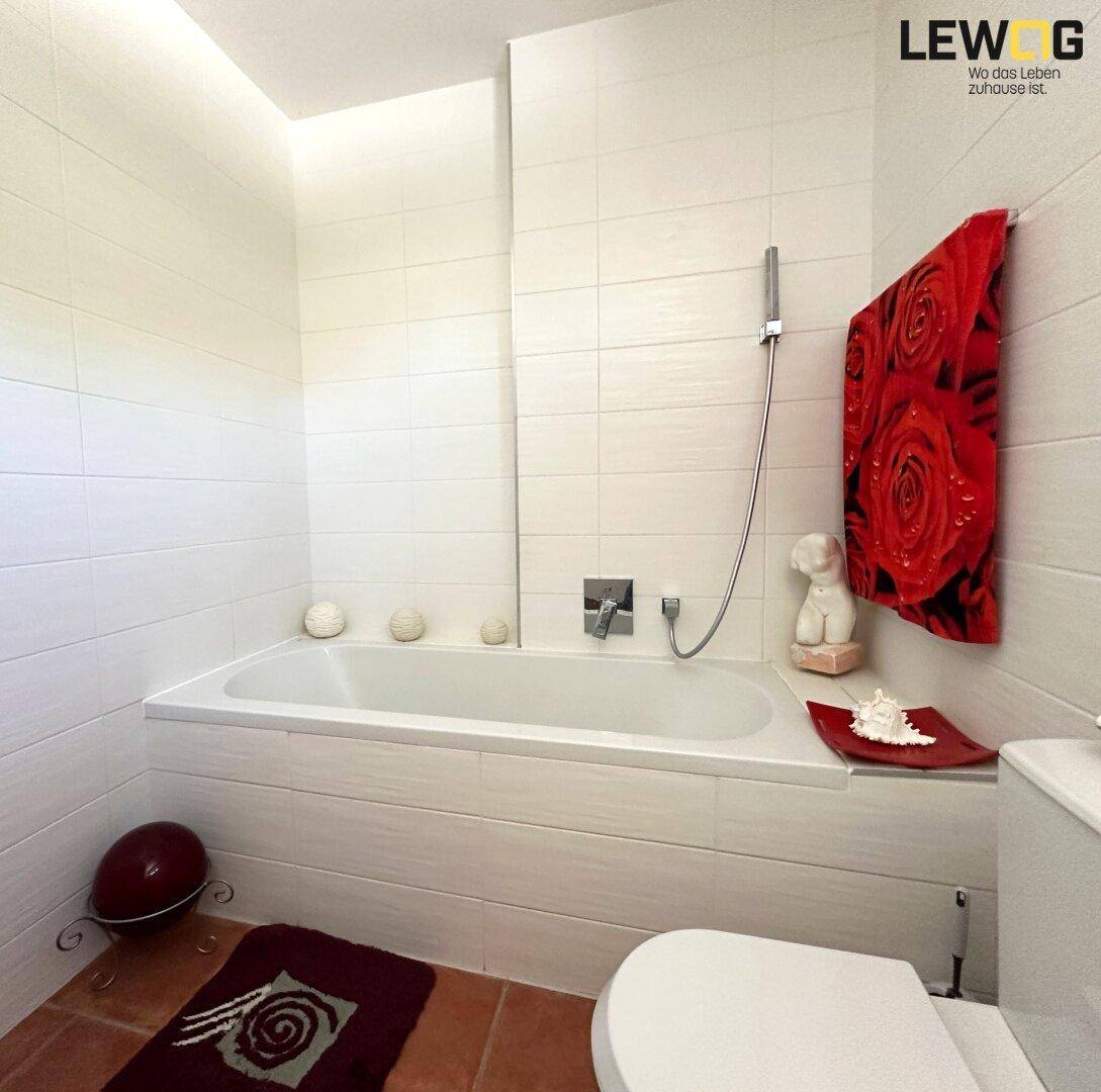 Modernes Badezimmer mit weißer Badewanne, Wandfliesen und Terrakotta-Bodenfliesen.