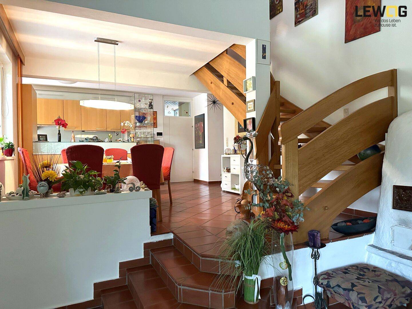 Großzügiger Wohn-Essbereich mit offener Küche, Holztreppe und traditionellem Kachelofen.