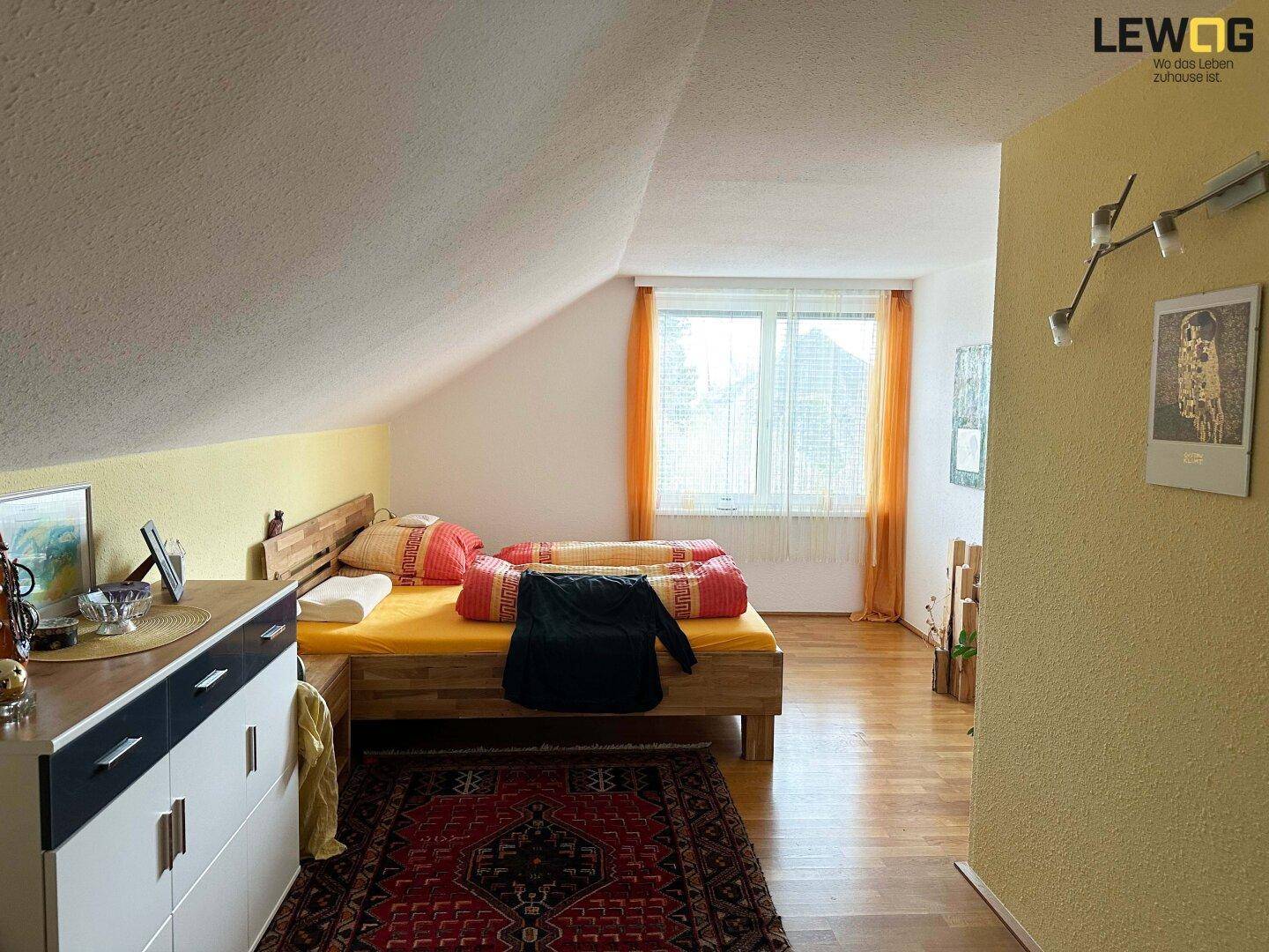 Helles Schlafzimmer im Dachgeschoss mit Holzbett, Laminatboden und schrägen Wänden.