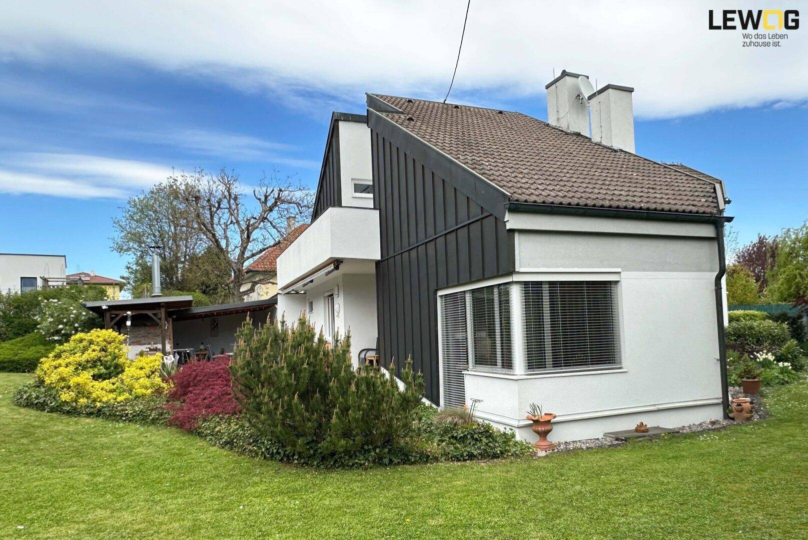 Seitenansicht des Hauses mit Satteldach, Erkerfenster und einem gepflegten Gartenbereich unter blauem Himmel.
