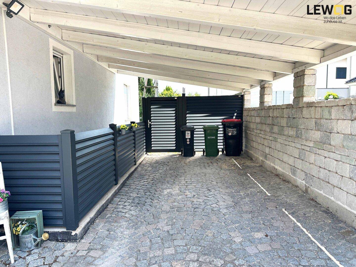 Überdachter Stellplatz mit Kopfsteinpflaster und Sichtschutzwand neben dem Haus.