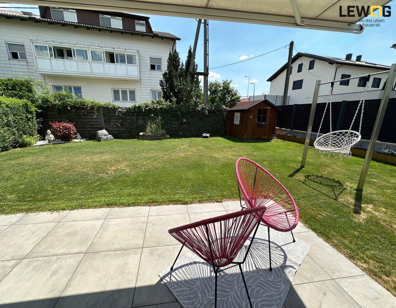 Grüner Garten mit Rasenfläche, Gartenhaus und gemütlicher Terrasse mit Sitzgelegenheiten.