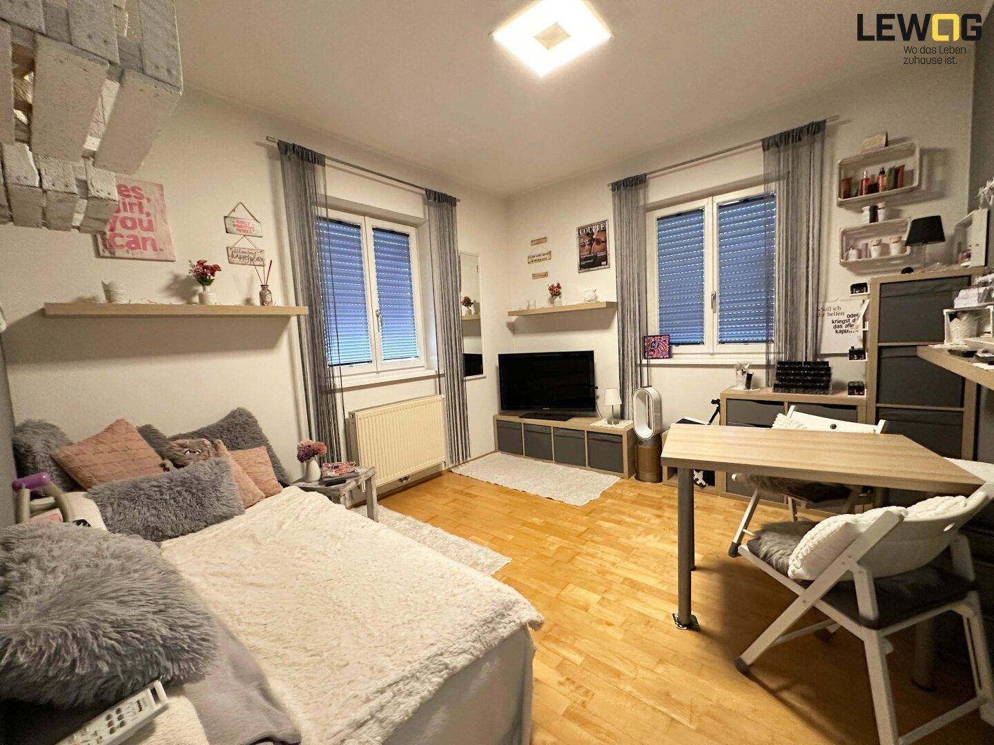 Helles Schlafzimmer mit Bett, Schreibtisch und Holzfußboden, ideal für Kinder oder Gäste.