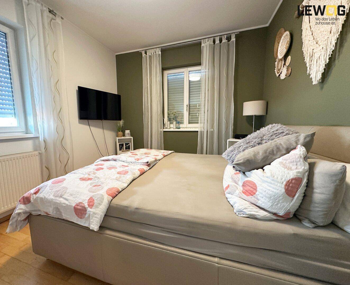 Helles Schlafzimmer mit Doppelbett, grüner Akzentwand und Holzparkettboden.