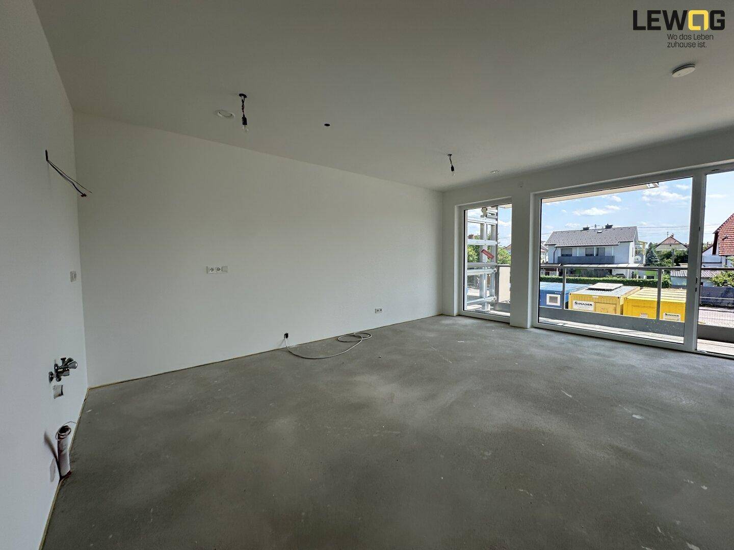 Heller, unmöblierter Wohnraum im Rohbau mit großen Fenstern und Betonboden.