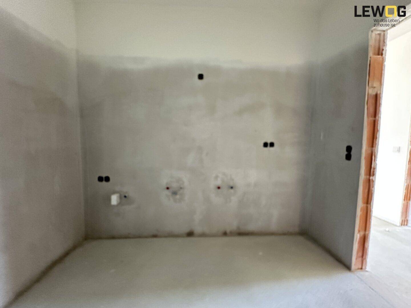 Unfertige Küche mit vorbereiteten Anschlüssen für Geräte und blanken Wänden, bereit für den Einbau.