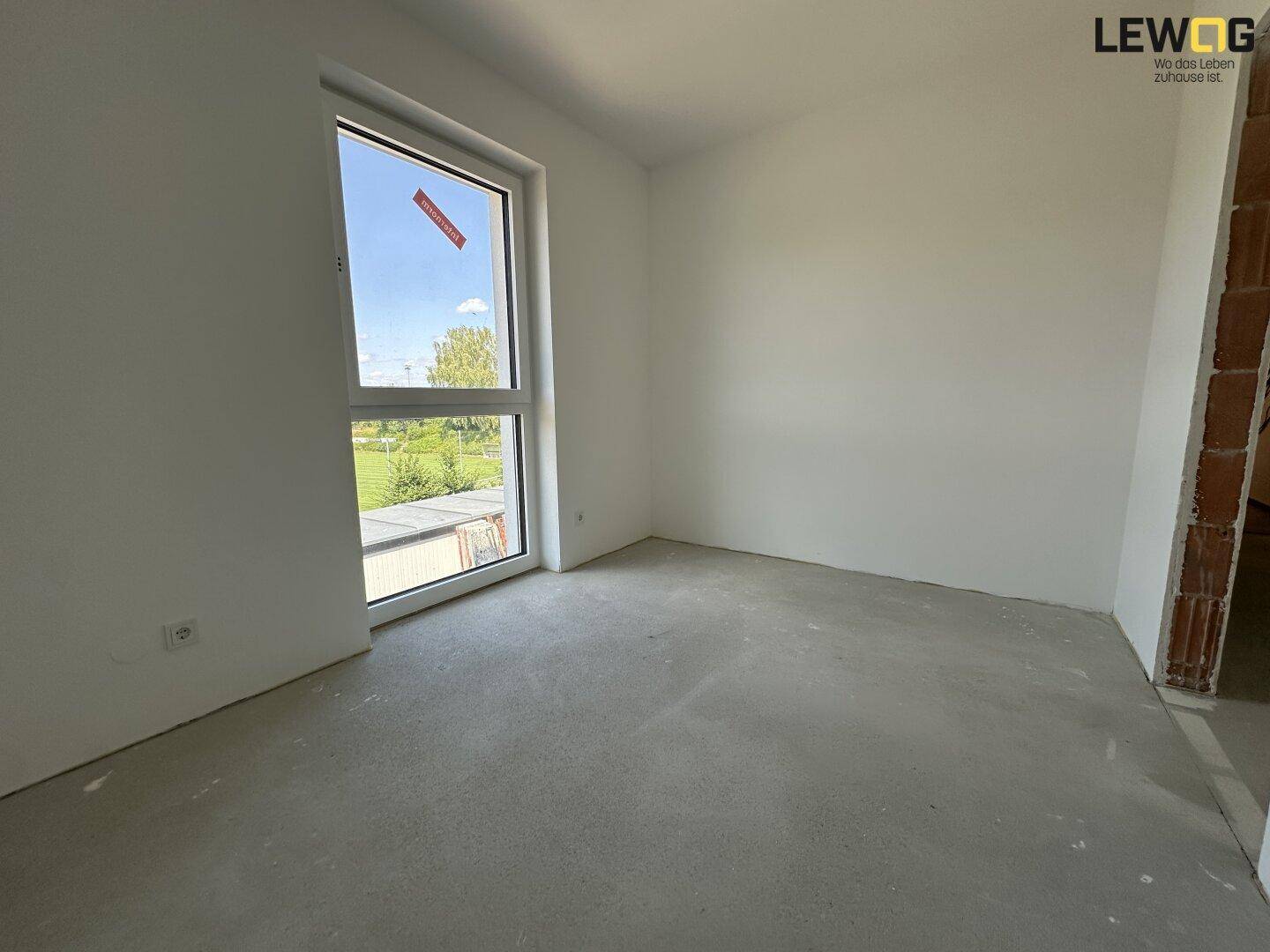 Heller, unfertiger Raum mit großem Fenster und Blick ins Grüne, bereit für den Innenausbau.
