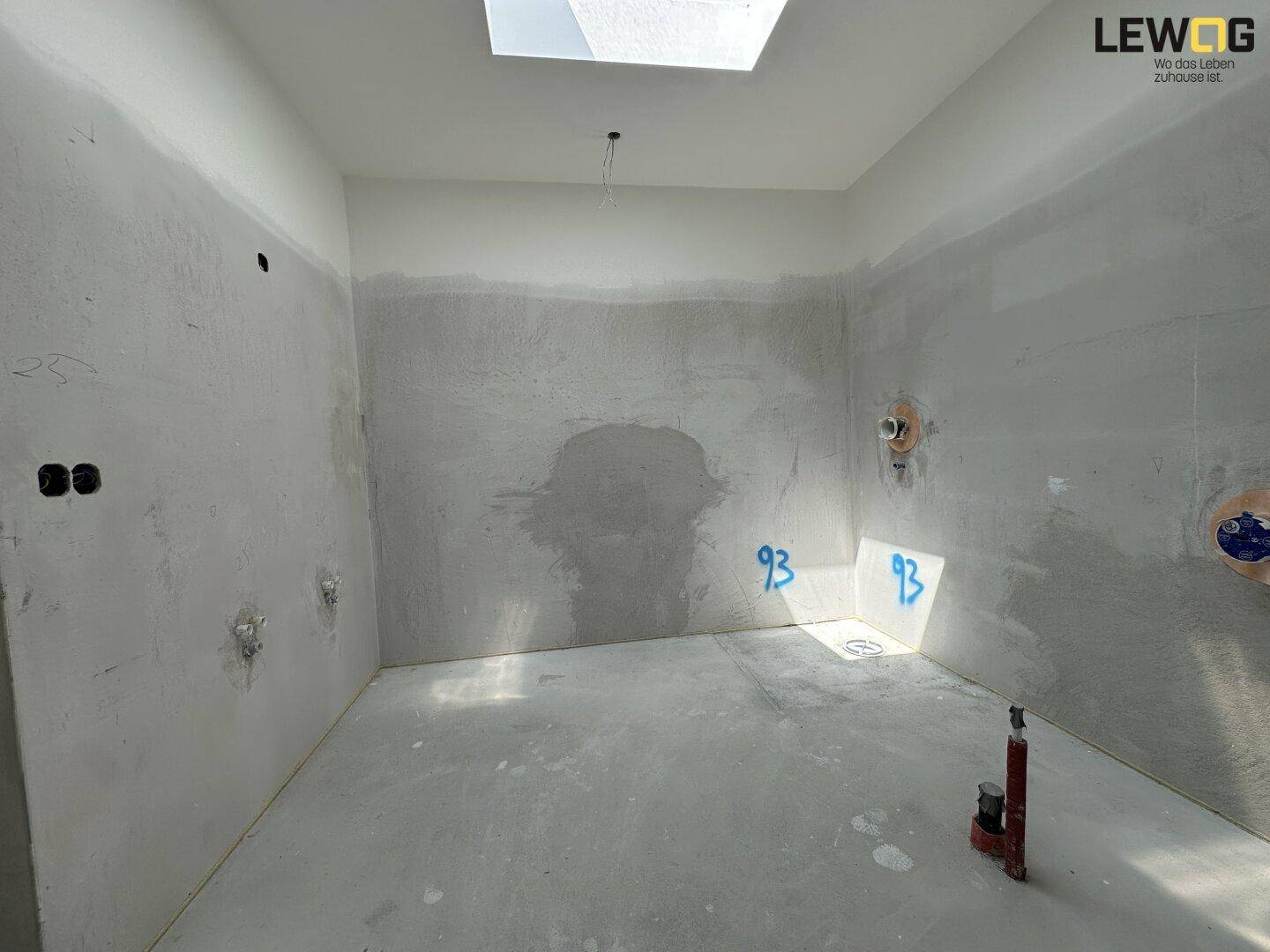 Unfertiges Badezimmer mit Rohinstallationen, Betonwänden und einem Oberlicht für natürliches Licht.