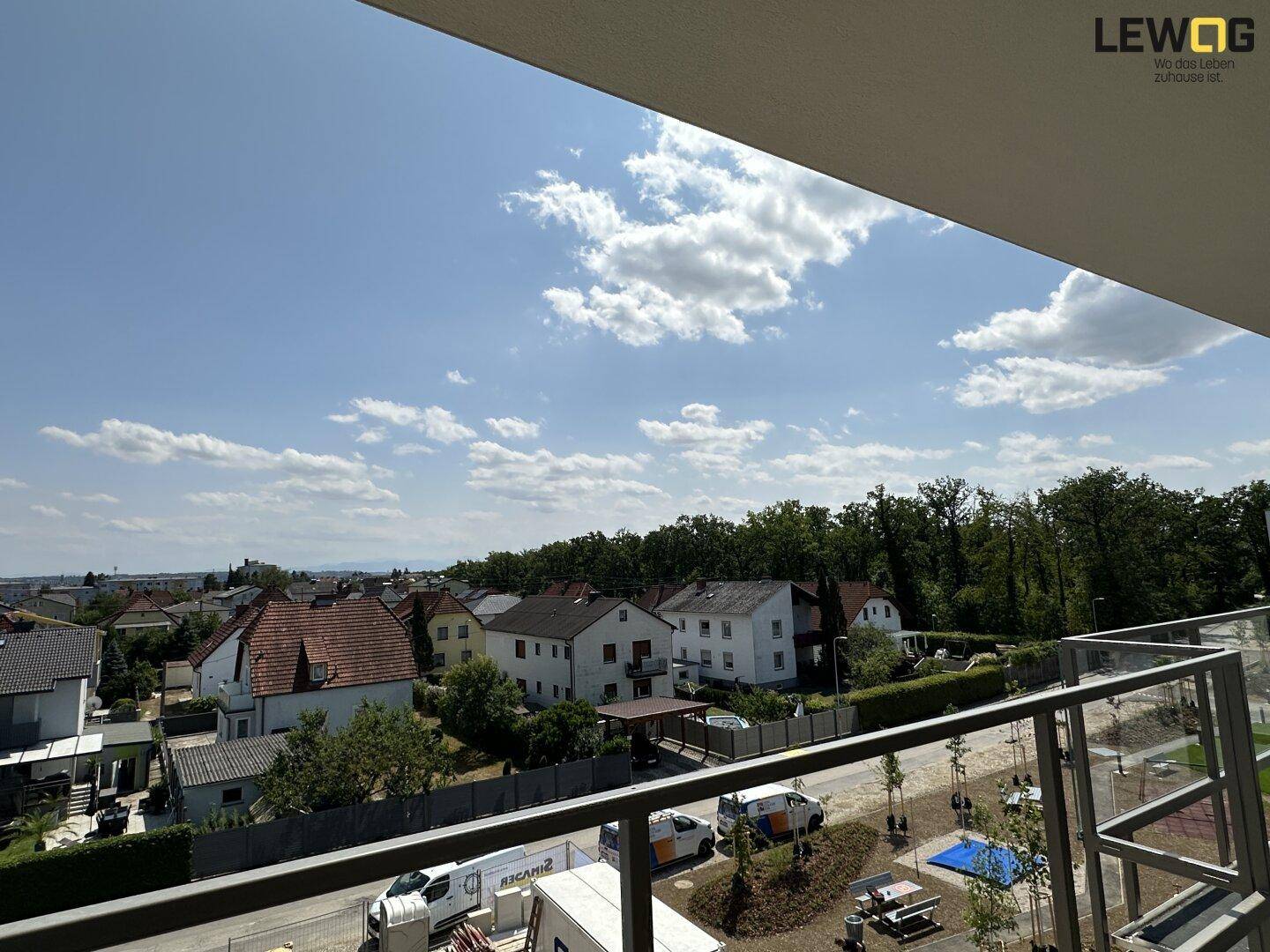 Weitblick von einem Balkon über eine Wohnsiedlung mit viel Grün und einem Baufeld.