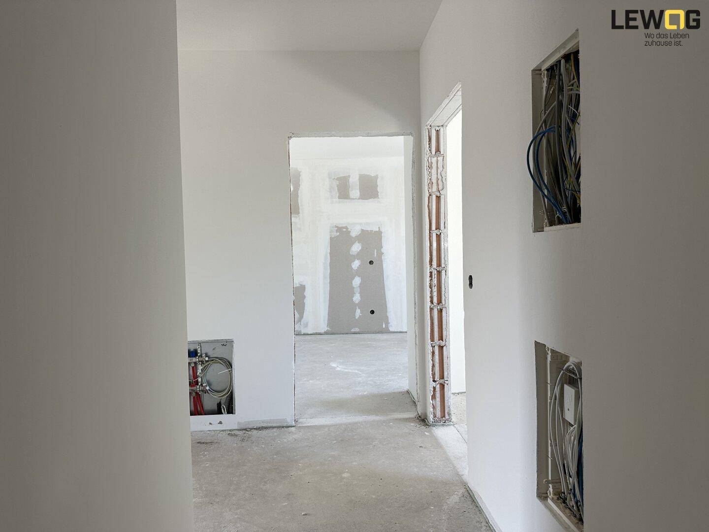 Unfertiger Flur in einem Neubau mit sichtbaren Elektroinstallationen und Rohbauwänden.