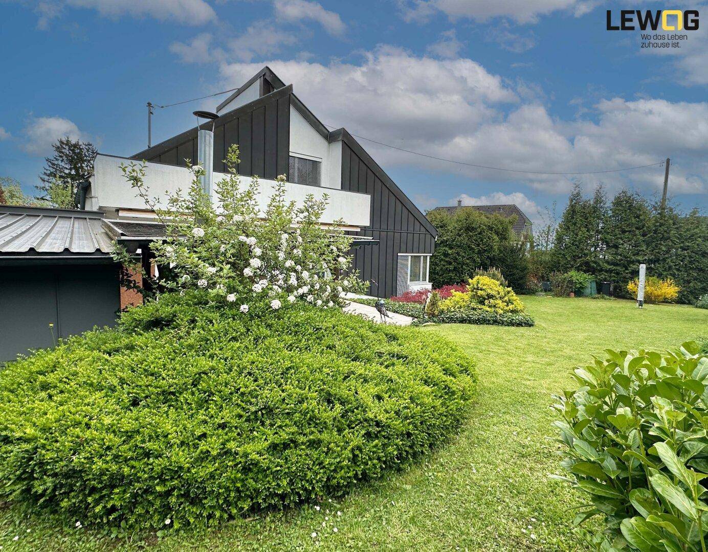 Weitläufiger Gartenbereich mit gepflegtem Rasen und blühenden Sträuchern vor moderner Hausfassade.