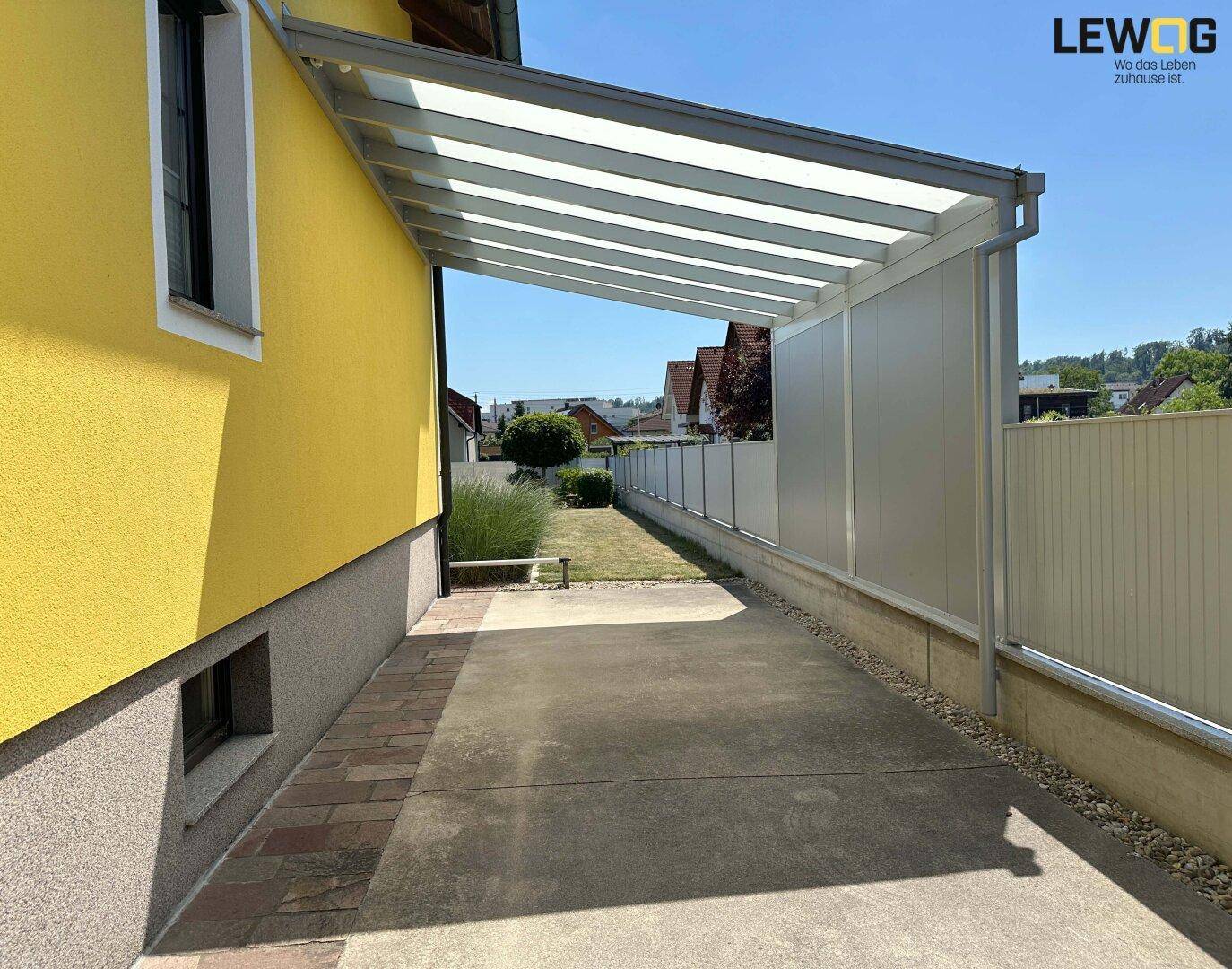 Überdachter Stellplatz neben dem Haus mit Zugang zum Gartenbereich.