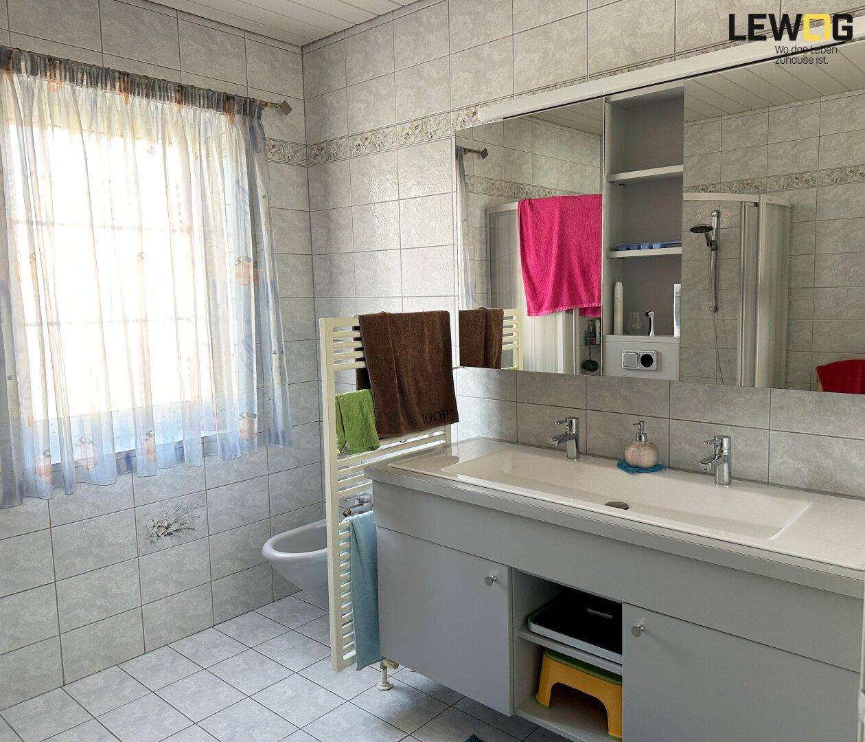 Helles Badezimmer mit Doppelwaschbecken, Spiegelschrank und Fenster.