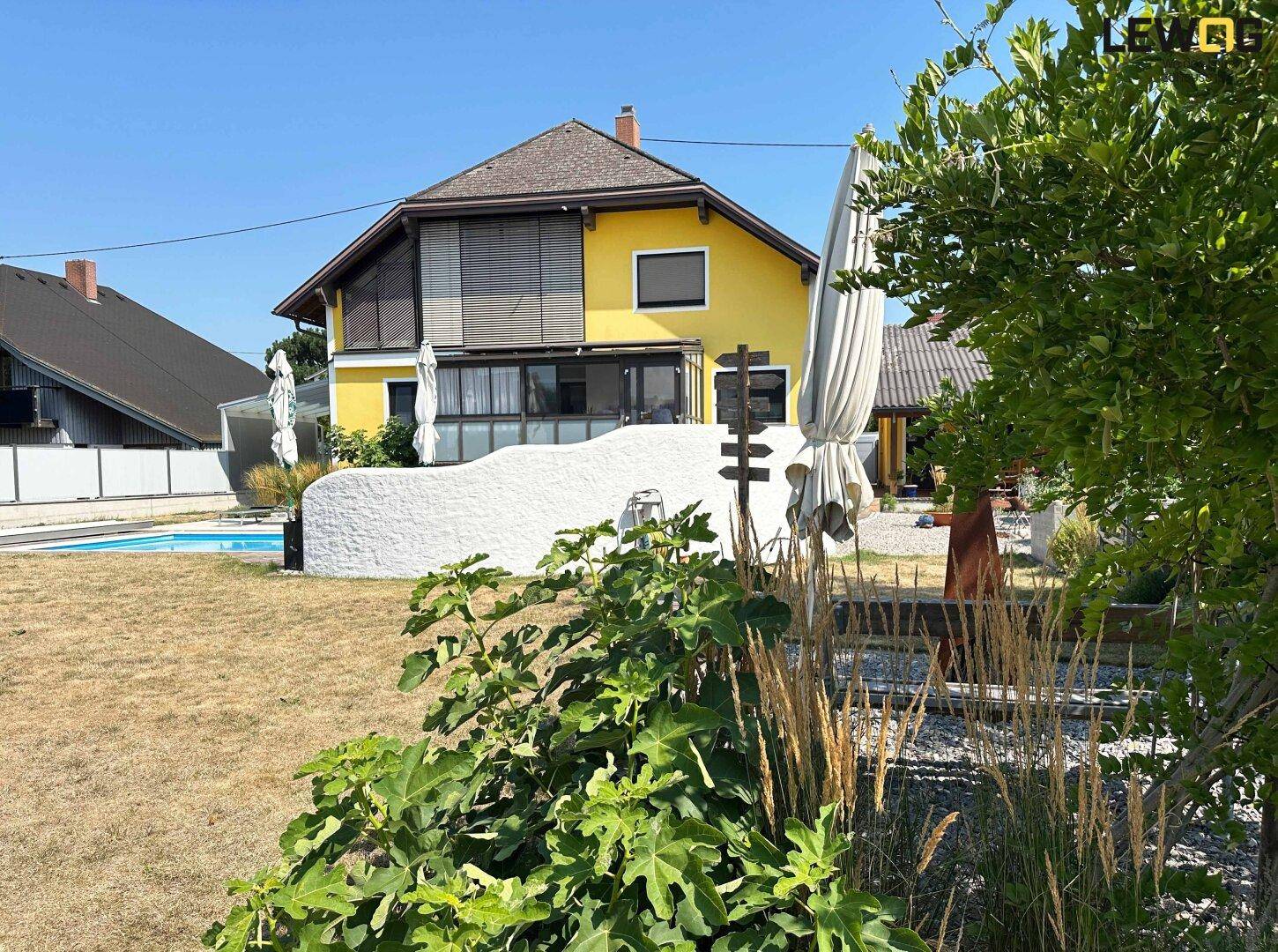Gelbes Haus mit weitläufigem Gartenbereich, Pool im Hintergrund und üppiger Bepflanzung.