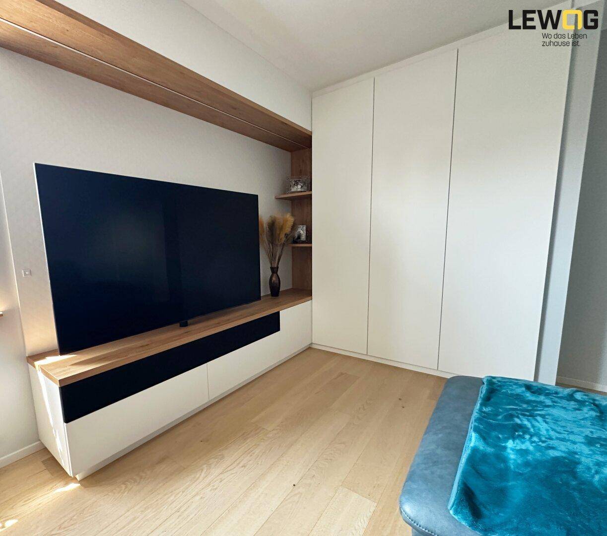 Wohnzimmer mit großem Fernseher, integrierten Schränken und hellem Holzfußboden.