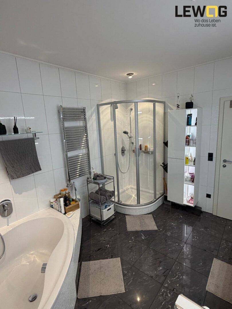 Helles Badezimmer mit weiß-dunklen Fliesen, Duschkabine, Badewanne und praktischem Handtuchheizkörper.