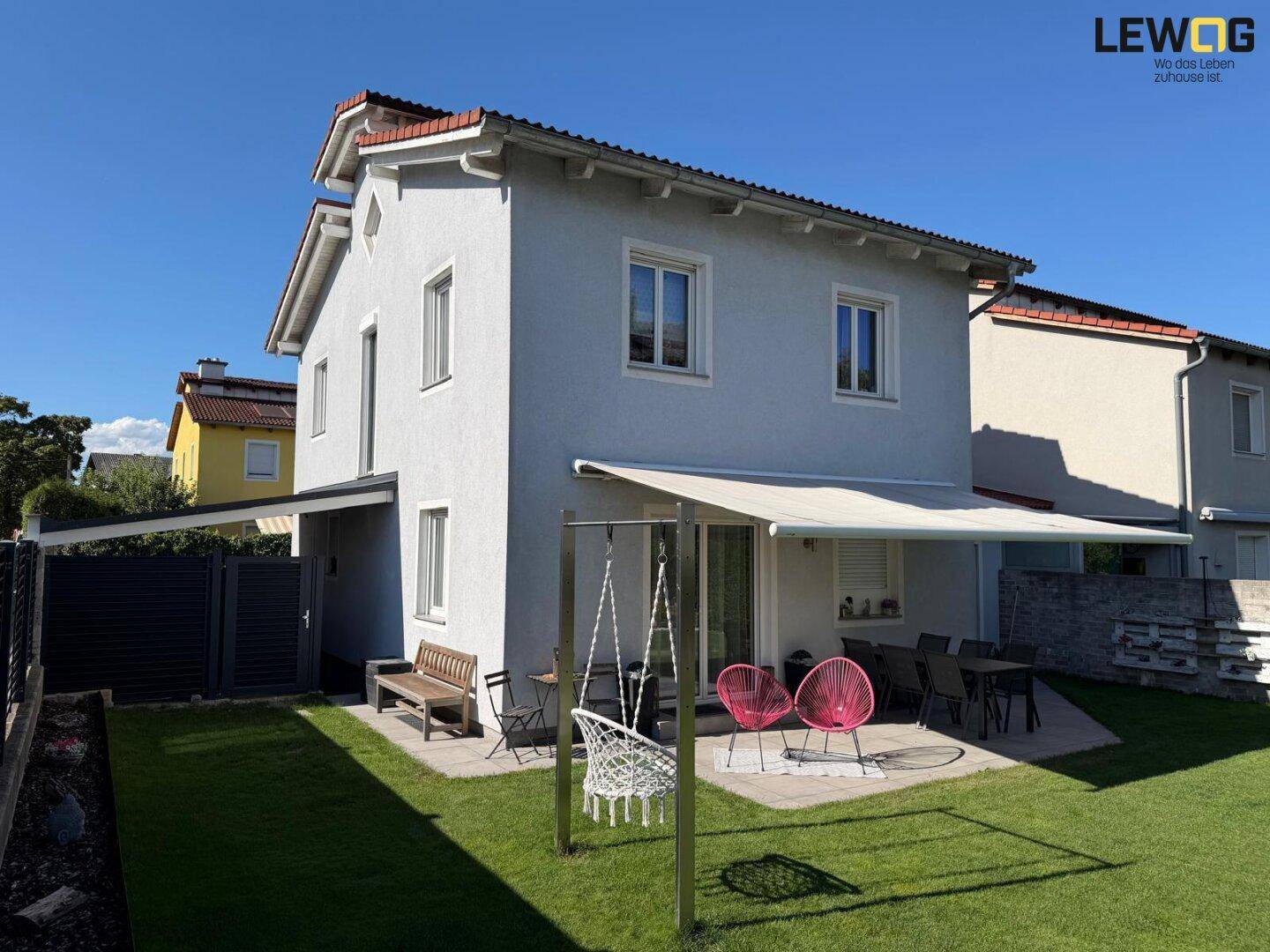 Gepflegter Hinterhof mit Rasenfläche, möblierter Terrasse und ausziehbarer Markise für angenehmen Schatten.