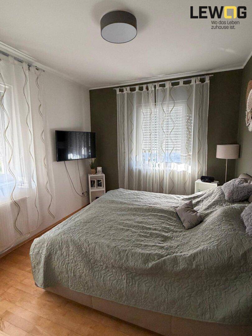 Gemütliches Schlafzimmer mit Doppelbett, hellem Laminatboden und zwei Fenstern für viel Tageslicht.
