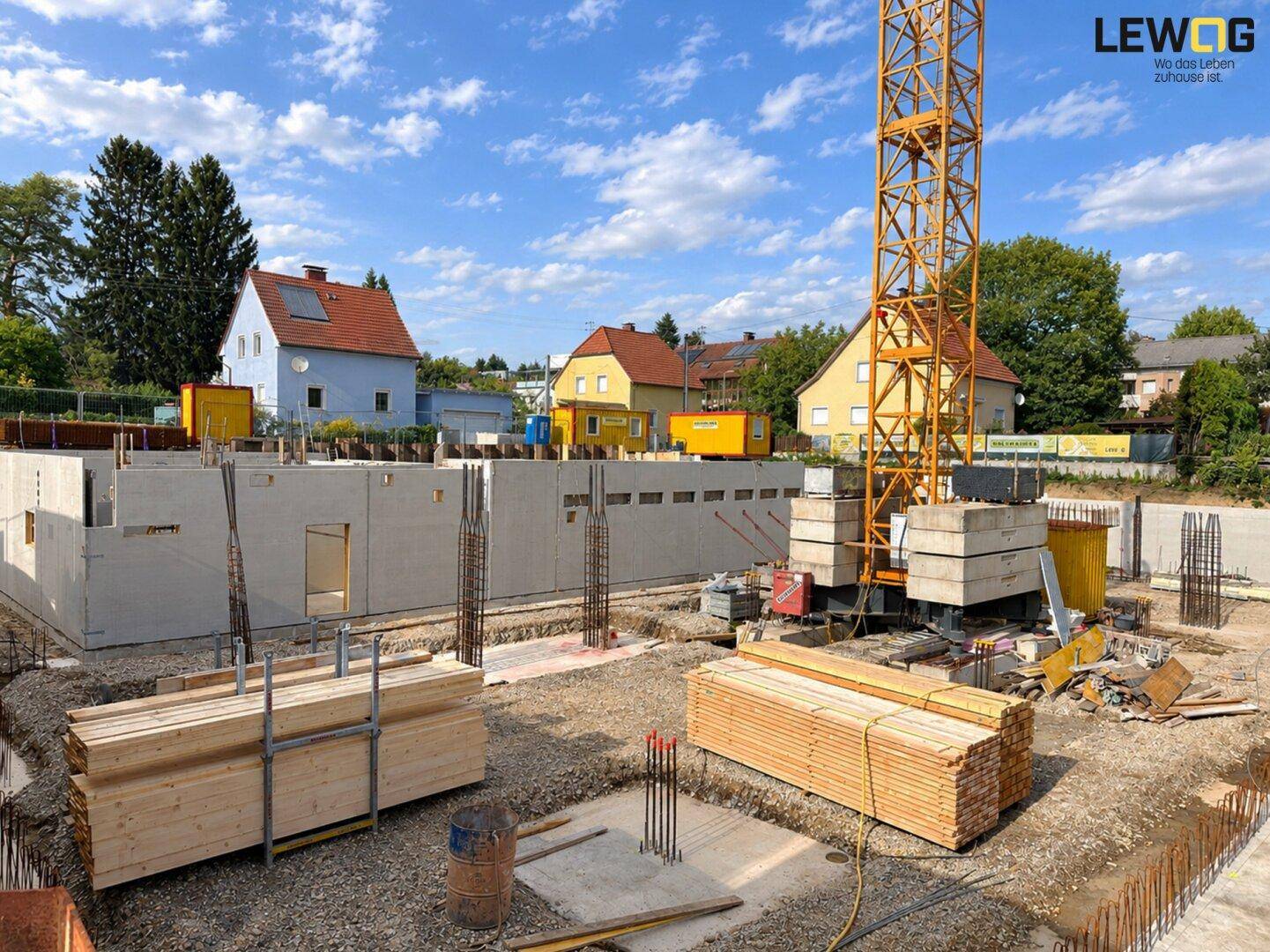 Baustelle mit bereits errichteten Fundamentmauern und einem Baukran unter blauem Himmel.
