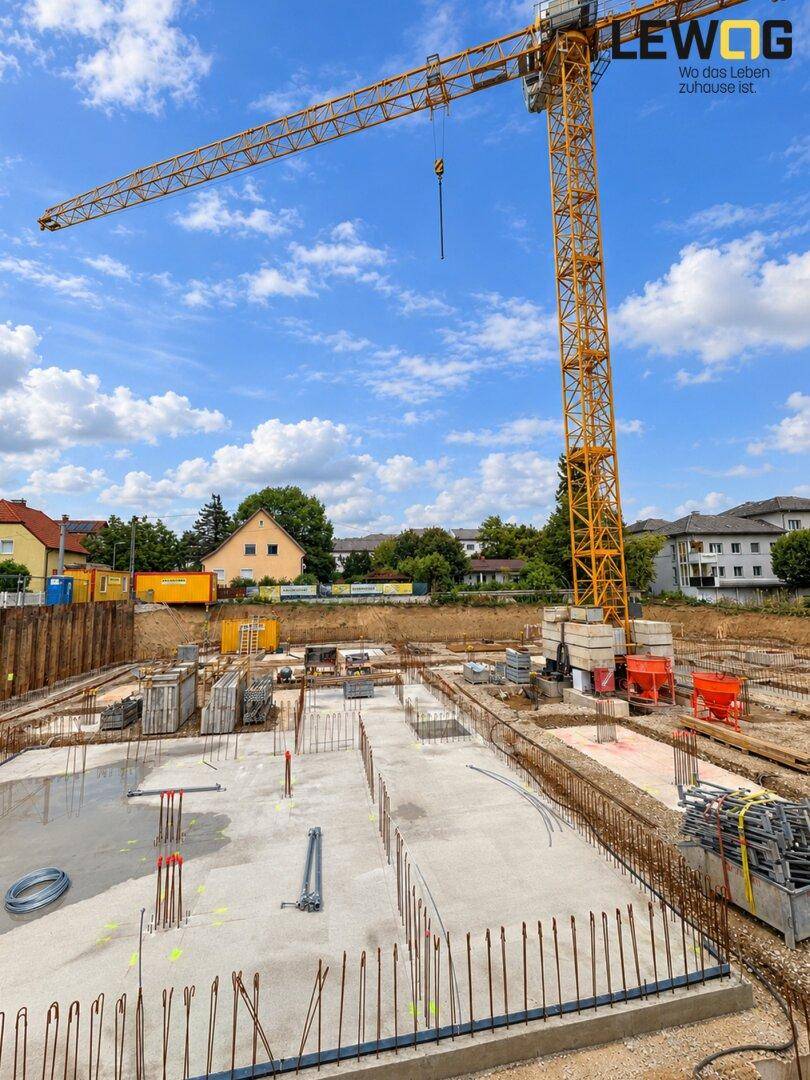 Baustelle mit ausgegossener Bodenplatte und einem großen Baukran unter strahlend blauem Himmel.