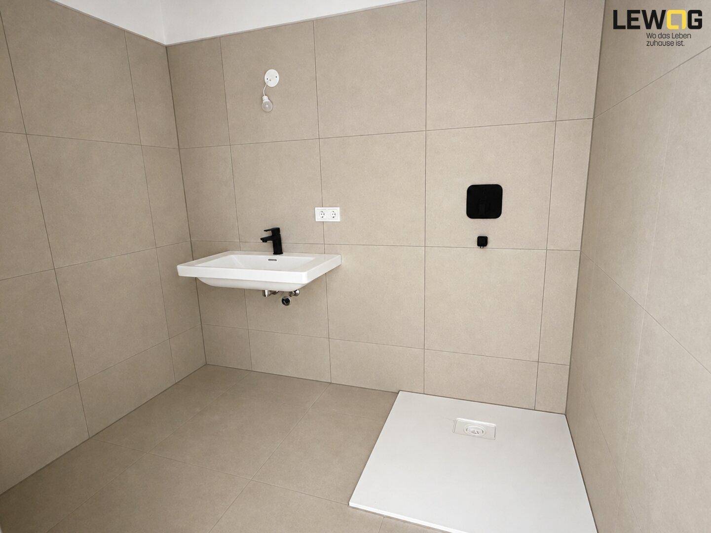 Modernes Badezimmer mit beigefarbenen Fliesen, wandhängendem Waschbecken und ebenerdiger Dusche.
