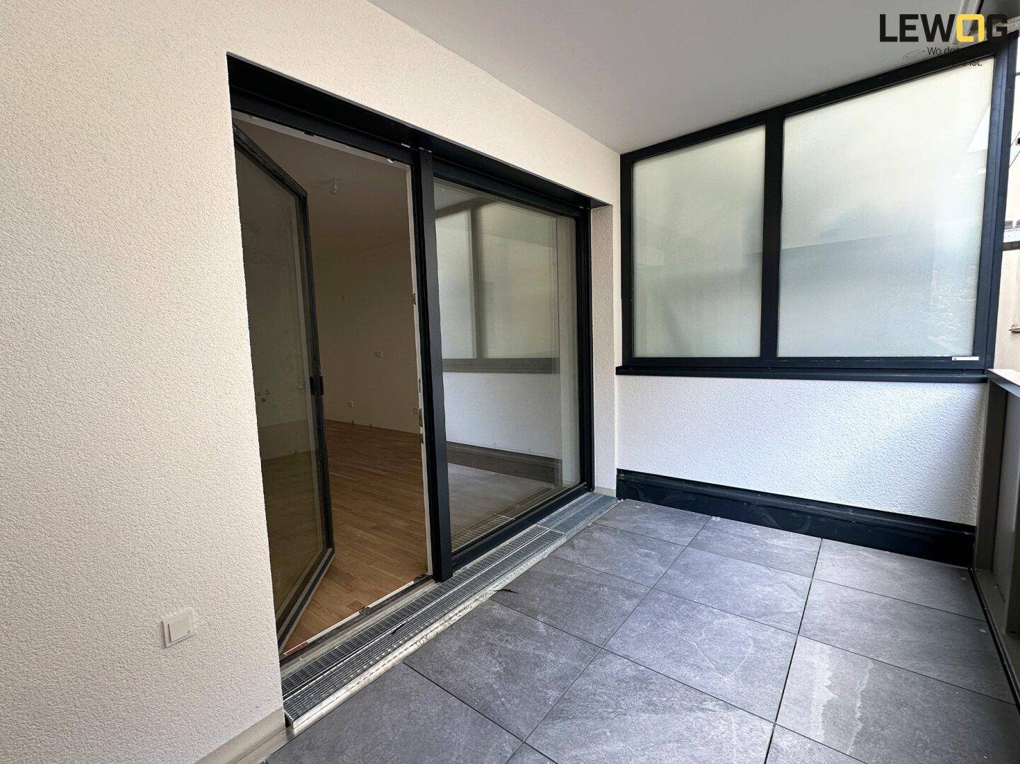 Moderner Balkon mit grauen Fliesen und großem Schiebetürzugang zum Innenraum.